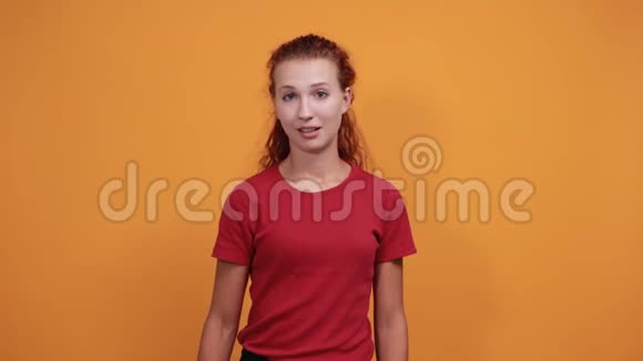 微笑的年轻女子穿着红色衬衫直指微笑着越过橙色的墙视频的预览图
