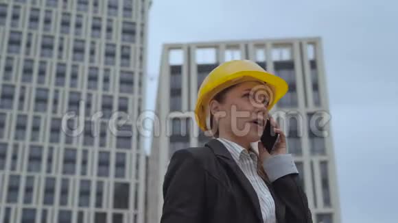 移动摄像头一个女人在一个建筑工地的背景下打电话穿商务夹克的女人视频的预览图