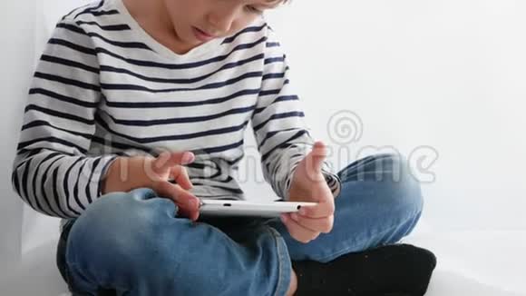 一个小男孩坐在窗户上用平板电脑为孩子们播放或看电影Z代概念视频的预览图