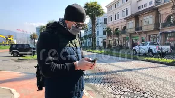 街上戴着口罩的男人在街上使用智能手机视频的预览图