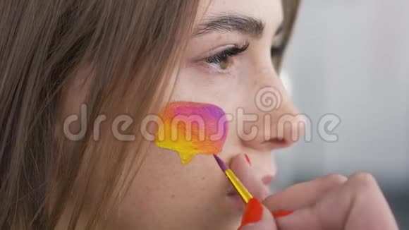 年轻可爱女人的特写肖像艺术家正在用小在女孩脸上画多色留言框视频的预览图
