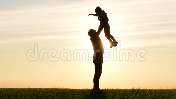 一个快乐的父亲在夕阳的背景下和他的孩子玩把它抛起来一个男人和一个孩子的剪影视频的预览图