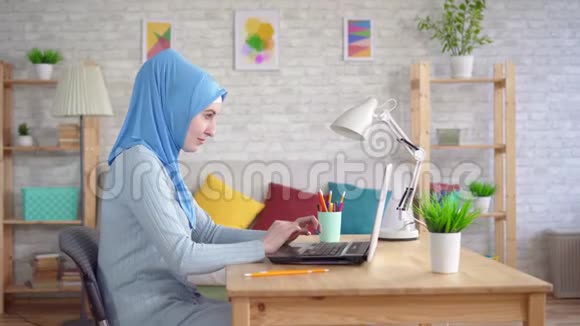 年轻的穆斯林妇女戴着国家头巾坐在笔记本电脑前视频的预览图
