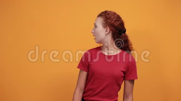穿红色衬衫的漂亮年轻女子看起来很高兴指着远处视频的预览图