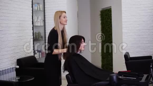 年轻漂亮的女人剪完头发后看着镜子理发师在客户面前挥舞着棕色长发视频的预览图