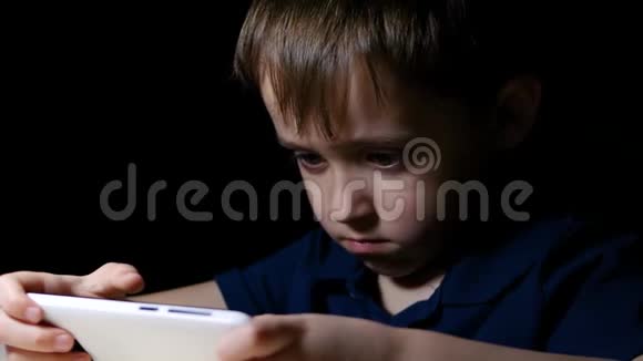 一个小男孩花时间在他的智能手机上看电影孩子在一个黑暗的房间里玩电话视频的预览图