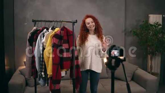 时尚红发的年轻女性vlogger正在为在线博客录制关于站在货架旁边的时髦衣服的视频视频的预览图
