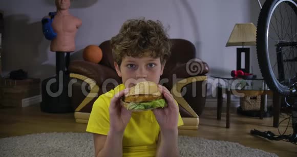 吸收白种人十几岁的男孩看电视咀嚼汉堡包开始咳嗽可爱的带垃圾的少年儿童画像视频的预览图