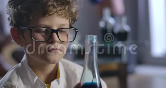 白人男孩拿着蓝色液体的瓶子和思考的肖像智能少年的特写脸视频的预览图