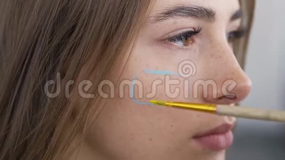 一个年轻漂亮女人的详细肖像艺术家用小软刷子在女孩脸上作画身体艺术视频的预览图