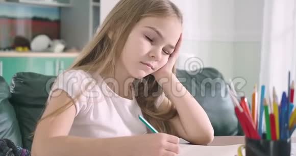 睡觉的白人女孩坐在桌子旁一只手拿着笔筋疲力尽的学童醒来后视频的预览图