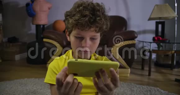 在智能手机屏幕上看电影的白人男孩的脸可爱的孩子有灰色的眼睛和卷发被视频的预览图
