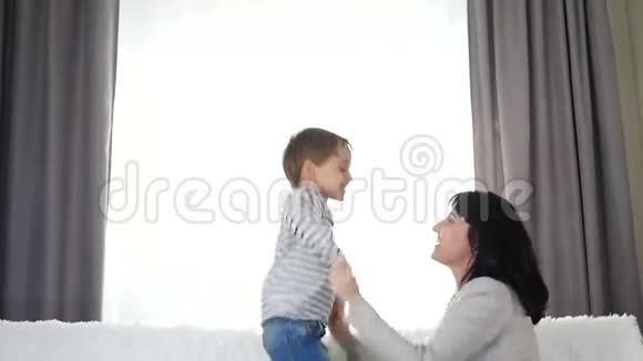 一个快乐的孩子抱着妈妈的手跳床上家人妈妈和儿子一起玩视频的预览图