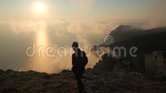 一位年轻女子沿着海边的悬崖边散步从高处观看美丽的戏剧性日落视频的预览图