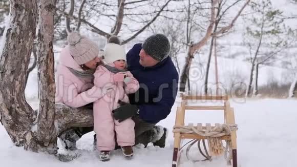穿着粉红色冬季连衣裙的小女孩在雪天上雪橇后吃圣诞姜饼可爱的家庭过冬视频的预览图