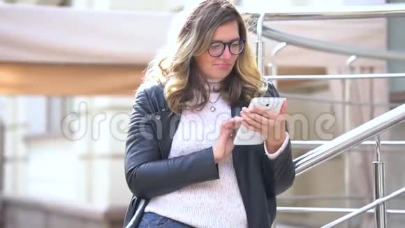 一个戴着眼镜的漂亮女孩站在栏杆旁边拿着智能手机和它一起工作美丽的人视频的预览图