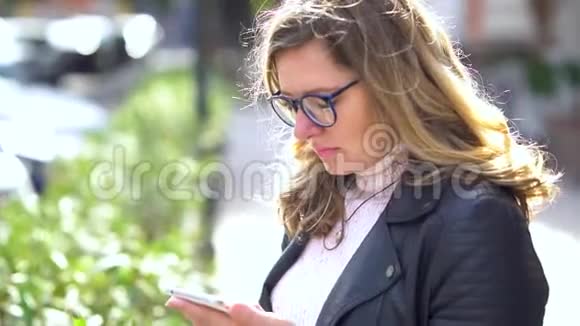 一个戴着眼镜的漂亮女孩站在树上带着智能手机微笑着和它一起工作美丽的人视频的预览图