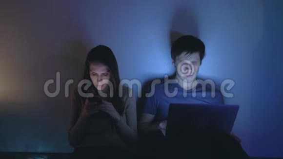 年轻夫妇晚上坐着用他们的电子设备交流视频的预览图