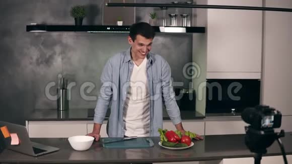 穿休闲服装的年轻人在灰色厨房里领导一个烹饪博客和录制视频博客的视频拍摄视频的预览图