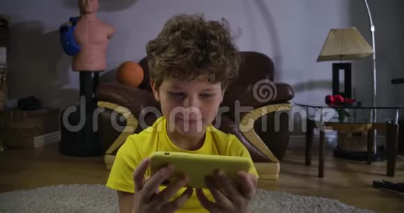在智能手机屏幕上看动画片或电影的专注白人男孩的脸卷毛的孩子被吸收视频的预览图