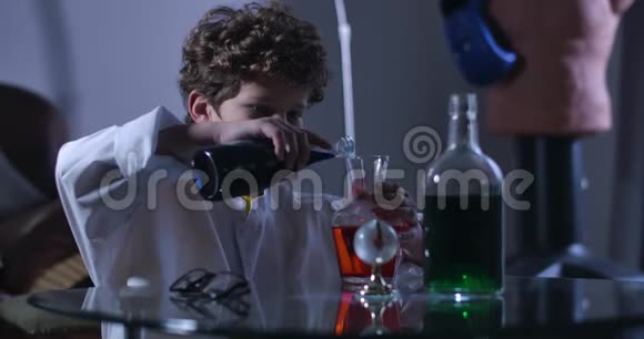白种人男孩在烧瓶中混合多种颜色液体的侧面视图穿着实验室外套的卷发少年天才视频的预览图