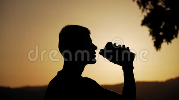 一个身材匀称的年轻人在日落时喝着带有太阳的水的轮廓视频的预览图