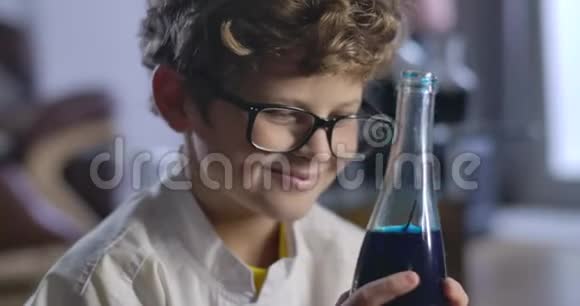 快乐的白人男孩的脸拿着蓝色液体和微笑的瓶子一个聪明的卷发少年的肖像视频的预览图