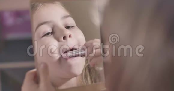 在镜子里看到可爱的高加索女孩涂口红微笑幼儿学习使用化妆面部护理视频的预览图