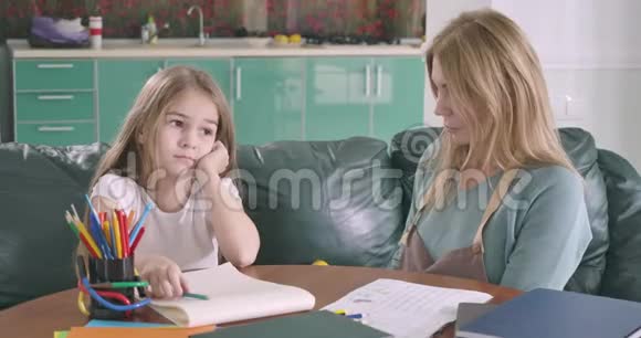 懒惰的白种人女孩坐在桌子旁不想学习年轻的母亲试图帮助女儿做家庭作业视频的预览图
