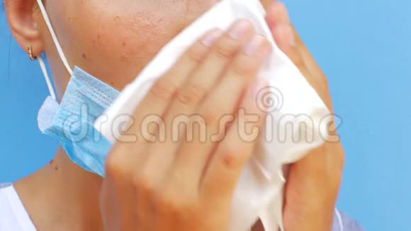 一个戴着面具的年轻女人用纸巾吹鼻子视频的预览图
