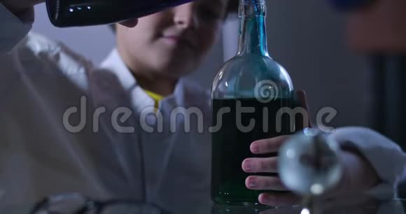 白种人男孩混合的烧瓶中液体的特写头发卷曲的少年穿着实验室外套手里拿着装满瓶子视频的预览图