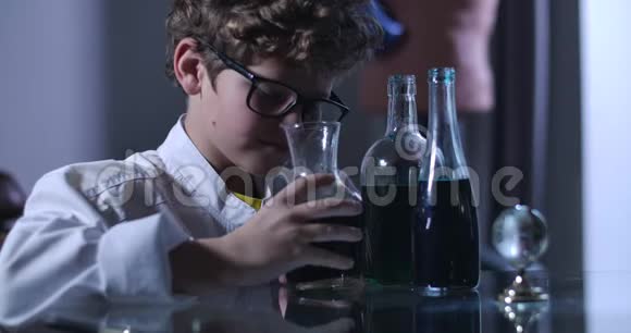 聪明的白种人男孩戴着眼镜和实验室外套看着装有液体的烧瓶年轻的青少年天才在他的视频的预览图