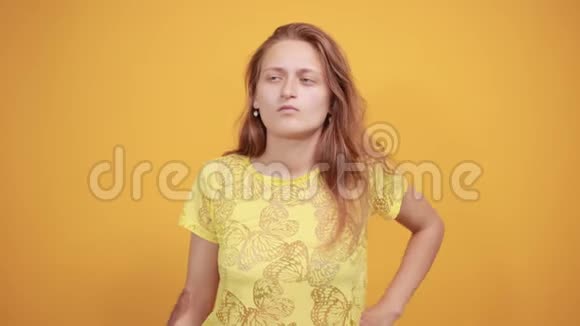 在橙色背景下穿黄色t恤的布鲁内特女孩表现出情感视频的预览图