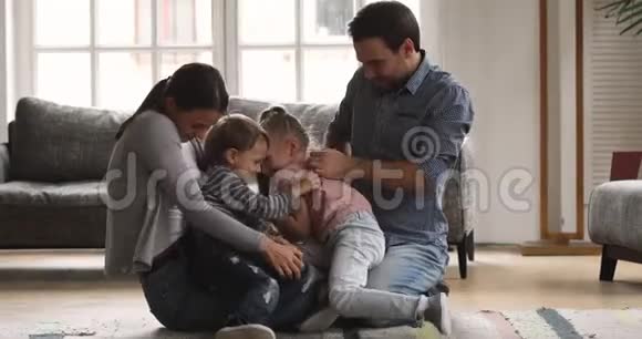 快乐的爸爸妈妈和孩子们玩耍在地板上笑得痒痒视频的预览图