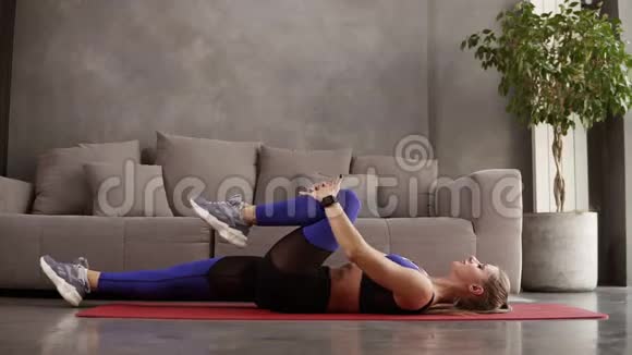 热身运动穿着运动服的漂亮的运动女人躺在垫子上腿抬到躯干上视频的预览图