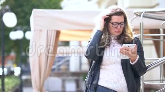 一个戴着眼镜的漂亮女孩站在街道上的栏杆旁戴着智能手机头发挺直美丽的人视频的预览图