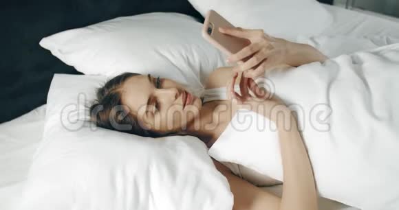 女人在床上使用智能手机视频的预览图