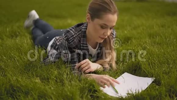 热情的女艺术家躺在草地上在笔记本上画画公园绿草如茵4K视频的预览图