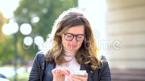 一个戴着眼镜的漂亮女孩站在街上拿着智能手机和它一起工作美丽的人视频的预览图
