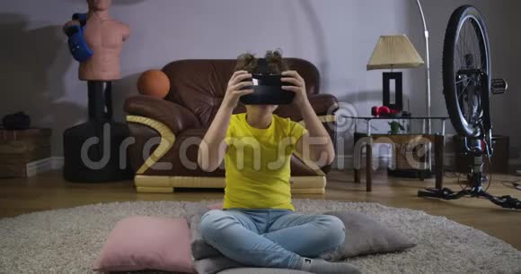 十几岁的白种人男孩在VR耳机坐在地板上在家里环顾四周不错的孩子尝试视频的预览图