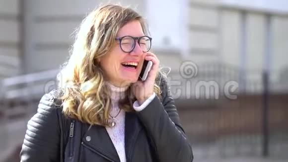 一个戴着眼镜的漂亮女孩站在智能手机旁微笑着视频的预览图
