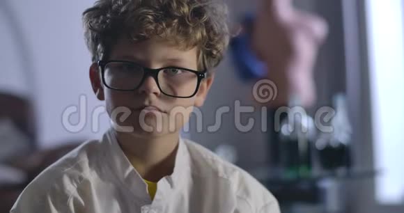 一个可爱的白人男孩的特写卷发脱下戴上眼镜聪明的少年看着摄像机视频的预览图