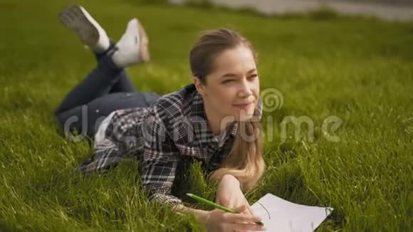艺术家女孩躺在草地上在笔记本上画画公园绿草4公里视频的预览图