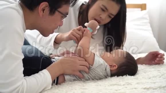 一家年轻的亚洲父亲和他的妻子温柔地亲吻他的小男孩的肚子视频的预览图