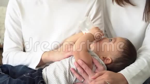 亚洲一家年轻的父亲和母亲用奶瓶喂养一个小男孩视频的预览图