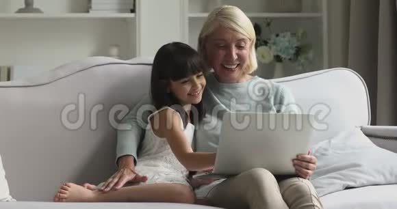 用手提电脑在沙发上笑着成熟的祖母和孙女视频的预览图