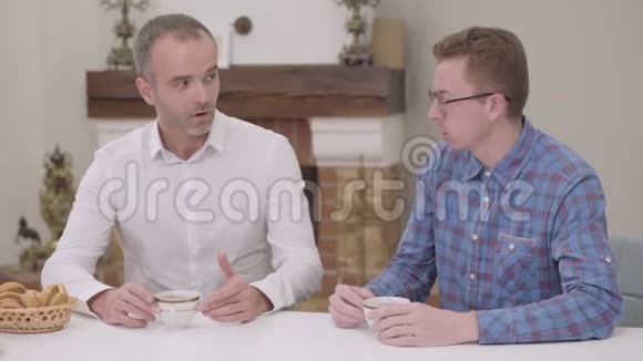 一个戴眼镜的白人男孩和坐在桌子旁的老人说话公公做出讽刺的表情视频的预览图