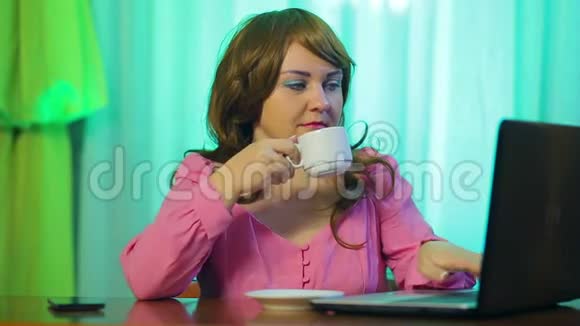 红发女人在咖啡馆的一张桌子上喝咖啡和一台电脑一起工作视频的预览图