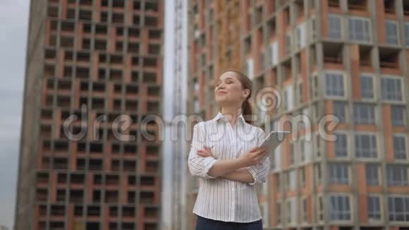 一个自信快乐的女人在一栋正在建造的多层建筑的背景下一个女人拿着一块平板电脑在她身上视频的预览图