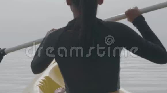 日出时一个苗条的女人坐在划桨船上划着皮划艇在海洋中活动视频的预览图